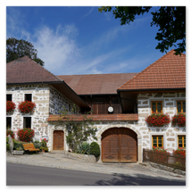 Traditionelles Steinbloßhaus mit roten Ziegeldächern, gelben Fensterrahmen, Blumenkästen und gepflastertem Zugang; ländliche Szene in Ottenschlag im Mühlviertel