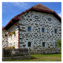 Traditionelles Steinbloßhaus mit weißer Fassade, Schindeldach, vergitterten Fenstern und kleinem Garten mit Holzzaun; ländliche Szene in Ottenschlag im Mühlviertel