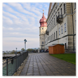 Perspektivischer Blick entlang der monumentalen barocken Palastfassade und der gepflasterten Aussichtsterrasse zum markanten rosa Zwiebelturm unter bewölktem Himmel.