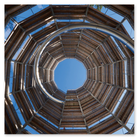 Aufwärtssicht im Baumwipfelpfad Grünberg: Eine spiralförmig gewendelte Holz- und Metall­konstruktion mit breitem Steg und Geländer führt durch Baumkronen zu einer offenen Decken­öffnung, durch die blauer Himmel sichtbar ist. Ideal für SEO-Stichworte wie Baumwipfelpfad Grünberg, Wipfelpfad, Treetop Walkway, Spiraltreppe, Holzarchitektur, Natur­erlebnis, Oberösterreich und Aussicht.