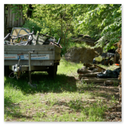 Anhänger mit Material und gestapeltem Brennholz entlang der Strecke Neumarkt–Unterweitersdorf, daneben Baumhaus und verstreute Arbeitsgeräte.