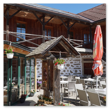 Gedeckter Gastgarten mit Tischen, Schirmen und Blumenschmuck vor Steinbloßhaus mit Holzaufbau; ländliche Szene in Ottenschlag im Mühlviertel