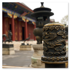 Detailreich verzierter Metallpfosten mit Drachenmotiv und Wolkenornamenten im Vordergrund; dahinter bronzene Tierfiguren und ein großer Räuchergefäß auf Sockeln, gerahmt von roten Säulen, vergitterten Fenstern und bemaltem Dach eines traditionellen chinesischen Bauwerks, die Szene verbindet symbolische Dichte mit architektonischer Tiefe.