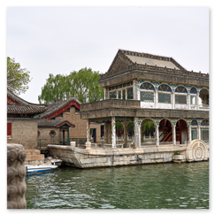 Lakeside-Pavillon in Bootsform mit Rundfenstern und dekorativem Radmotiv am Ufer des Kunming-Sees; davor Steinbrücke mit verzierten Geländern, dahinter Gebäude mit Ziegeldächern, die Szene verbindet kaiserliche Gartenarchitektur mit ruhiger Uferlandschaft.