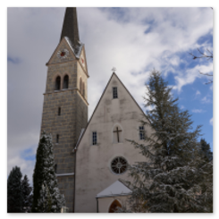 Kirche mit hohem Turm in Gosau, verschneite Landschaft, teils bewölkter Himmel