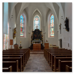 Kirchenschiff mit Altar, drei bunten Fenstern, Holzbänken und Figuren an den Wänden