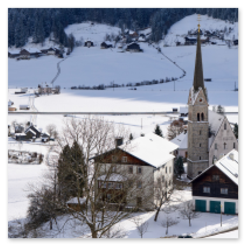 Verschneites Dorf in Gosau mit Kirche, traditionellen Häusern und bewaldeten Hügeln im Hintergrund