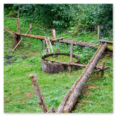 Eine historische Wasserkonstruktion aus Holz steht inmitten einer grünen Landschaft beim Burgbauprojekt in Friesach. Ein hölzerner Trog und ein einfaches Leitungssystem aus ausgehöhlten Baumstämmen zeigen, wie Wasser früher gelenkt und genutzt wurde. Die Szene vermittelt nachhaltige Technik und die kreative Nutzung natürlicher Materialien im mittelalterlichen Alltag.