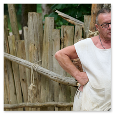 Person in mittelalterlicher Kleidung lehnt an rustikalem Holzzaun, umgeben von Waldkulisse beim Burgbauprojekt in Friesach