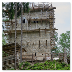 Steinturm mit Holzgerüst im Bau, umgeben von Wald, Teil des mittelalterlichen Burgbauprojekts in Friesach