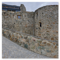 Steinbau mit Rundturm und kleinen Fenstern, moderner Anbau im Hintergrund, gepflasterter Weg mit Steinmauer im Vordergrund