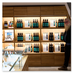 Innenansicht mit beleuchteten Regalen voller Flaschen, Glasvitrine mit Produkten und Besucher im Verkaufsraum des Weinguts Taggenbrunn