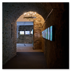 Steinkorridor mit gewölbter Decke und digitalen Bildschirmen an der Wand, führt zu Ausstellungsraum mit Leuchtschirmen und Kronleuchter, Teil der André-Heller-Installation im Weingut Taggenbrunn
