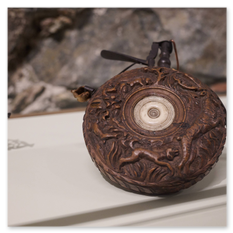 Rundes Holzobjekt mit Drachenmotiv und zentralem Inlay, Lederbänder an den Seiten, ausgestellt vor Steinwand in der historischen Sammlung auf Burg Taggenbrunn