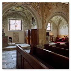 Innenraum mit Steinbögen, Glasfenstern und Seitenkapelle bei Maria Saal – Holzbank, Altarfigur und rote Stühle im Nebenraum, ruhige Lichtführung auf Steinboden.