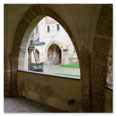 Steinbogen mit Blick auf gepflasterten Hof bei Maria Saal – Spitzbögen, Gittertor und Brunnenstruktur, ruhige Raumstaffelung zwischen sakraler Tiefe und Dorfarchitektur.