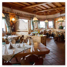 Gastraum im Gipfelhaus Magdalensberg mit Holzdecken, Herzstühlen und Fliesenboden – Tischdekoration, Glaslampen und Fenster mit grünen Vorhängen im warmen Innenraum.