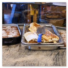 Drei Tabletts mit Gebäck im Gipfelhaus Magdalensberg – Staubzuckerkugeln, Strudelscheiben und Streuselkuchen auf Theke, Servierbesteck und Küchenumgebung im Hintergrund.