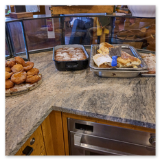 Buffetauslage mit Gebäck im Gipfelhaus Magdalensberg – Staubzuckerkugeln, Strudel, Blechkuchen und frittiertes Gebäck hinter Glas, Theke mit Granitplatte im Gastraum.