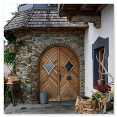 Eingangsbereich des Gipfelhauses Magdalensberg mit Holzportal, Steinfassade und Dekoration – Geweih, Blumen, Korb und Holzstücke vor weißer Wand mit Fensterrahmen.