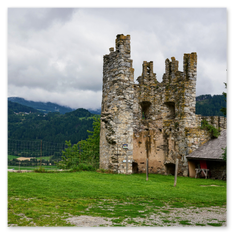 Teilruinierter Burgturm mit Holzunterstand und Baum in Friesach – Steinmauer mit Zinnen, Hügellandschaft im Hintergrund, Nebel über Tal und Feldern, ruhige Szene.