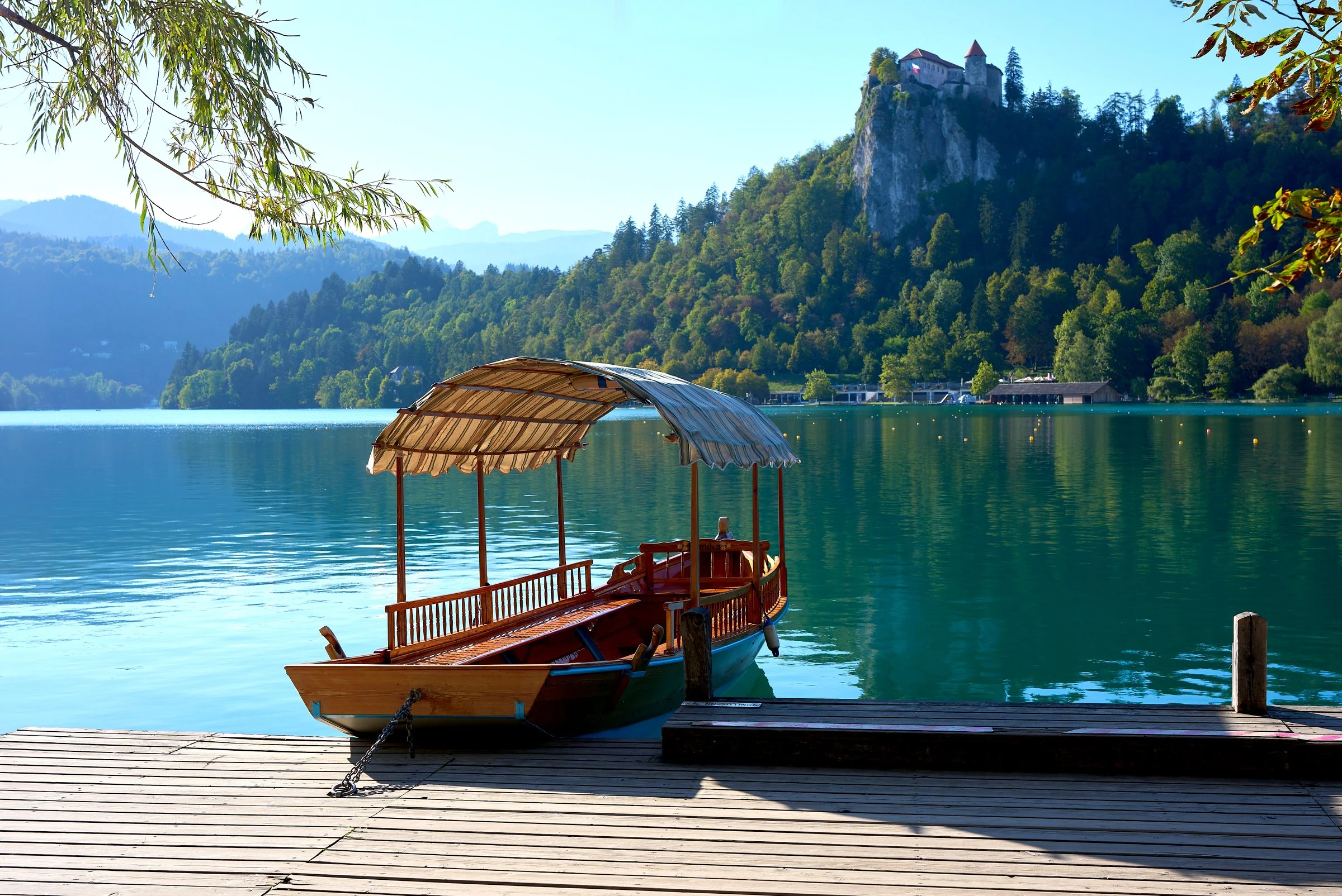 Aufnahme vom Ufer des Bleder Sees mit einem typischen Holzboot am Steg und der Burg Bled im Hintergrund.<br />