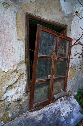 Zerfallenes Mauerstück mit offenem, beschädigtem Holzfenster; Spuren von Verlassenheit und Witterung
