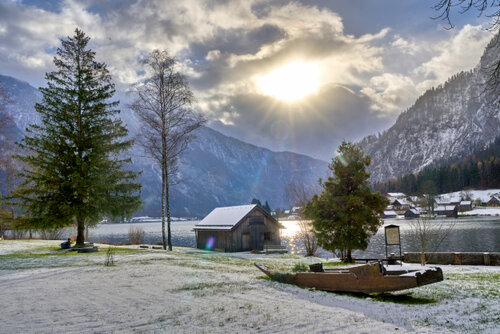 Bei fast bedecktem HImmel scheint die Sonne durch eine Wolke und vermittelt einen schönen Augenblick auf die teils beschneite Wiese auf der ein Boot am Ufer liegt.
