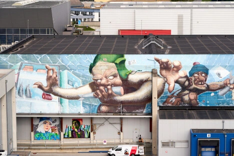 Großes Wandbild mit zwei cartoonhaften Figuren und Porträts darunter – farbige Gestaltung an Industriehalle im Hafenpark LINZ AG, als ruhiger Ort zum Betrachten.