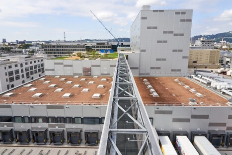 Luftbild eines großen Logistikzentrums mit Flachdächern, Verbindungsbrücke und Laderampen – industrielle Anlage im Hafenpark LINZ AG, ruhig zu betrachten