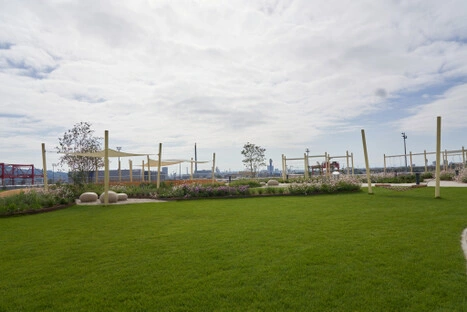Gepflegte Rasenfläche mit Blumenbeeten, Steinbänken und Stadtpanorama im Hintergrund – ruhiger Ort im Hafenpark LINZ AG zum Liegen und Verweilen