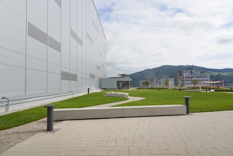Moderne Außenanlage mit Rasen, Kiesweg, Betonbänken und Blick auf Hügellandschaft – ruhiger Ort im Hafenpark LINZ AG zum Liegen und Verweilen