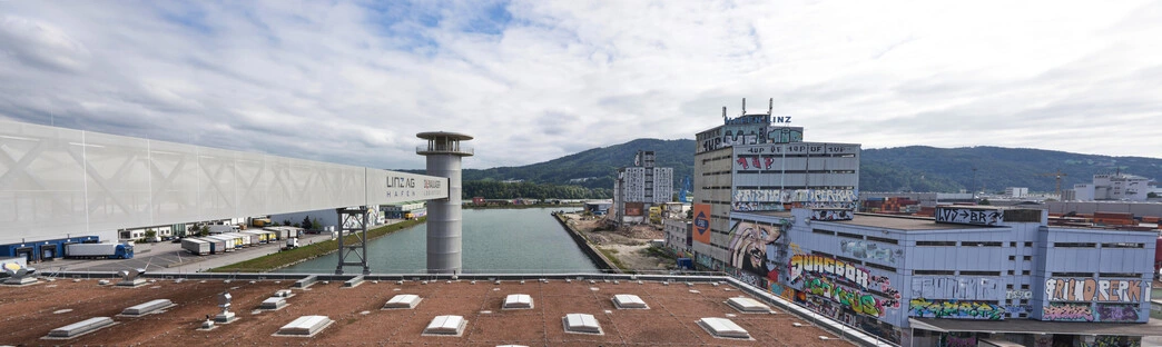 Zwischen Kanal, Lagerhallen und bemalten Gebäuden entsteht ein urbaner Kontrast; die Szene verbindet industrielle Infrastruktur mit farbiger Ausdruckskraft und Weitblick.