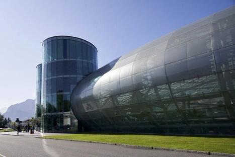 Futuristischer Glas- und Stahlbau des Red Bull Hangar-7 in Salzburg mit geschwungener Dachkonstruktion, Heimat historischer Flying-Bulls-Flugzeuge, Kunstausstellungen und gehobener Gastronomie, gelegen direkt am Flughafen vor alpiner Kulisse.